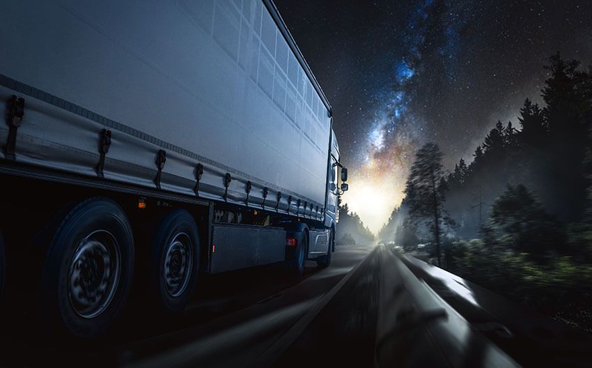 A semi truck is driving down a highway at night.