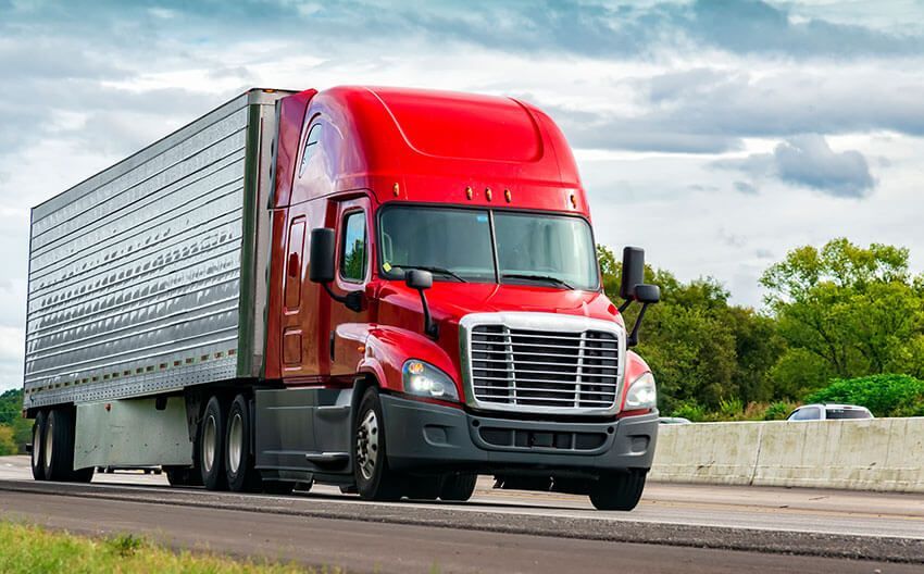 A red semi truck is driving down a highway.