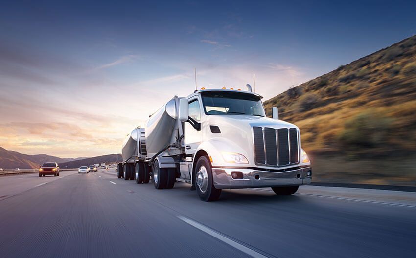 A semi truck is driving down a highway at sunset.