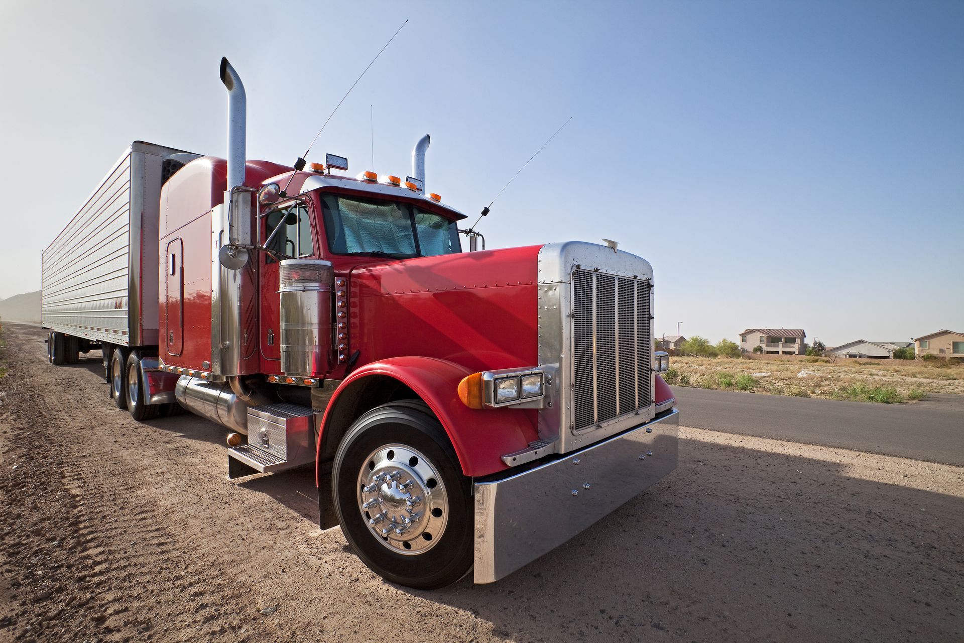 A red semi truck is parked on the side of a dirt road.