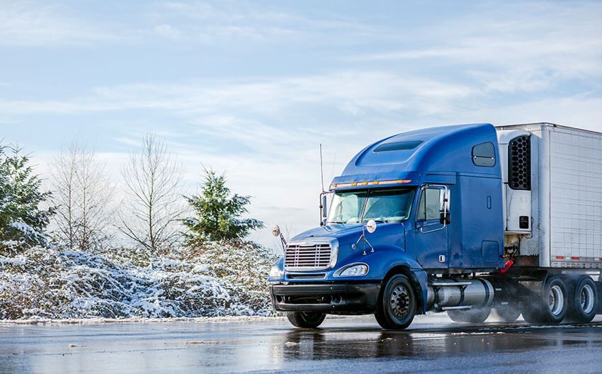 A blue semi truck with a white trailer is driving down a wet road.