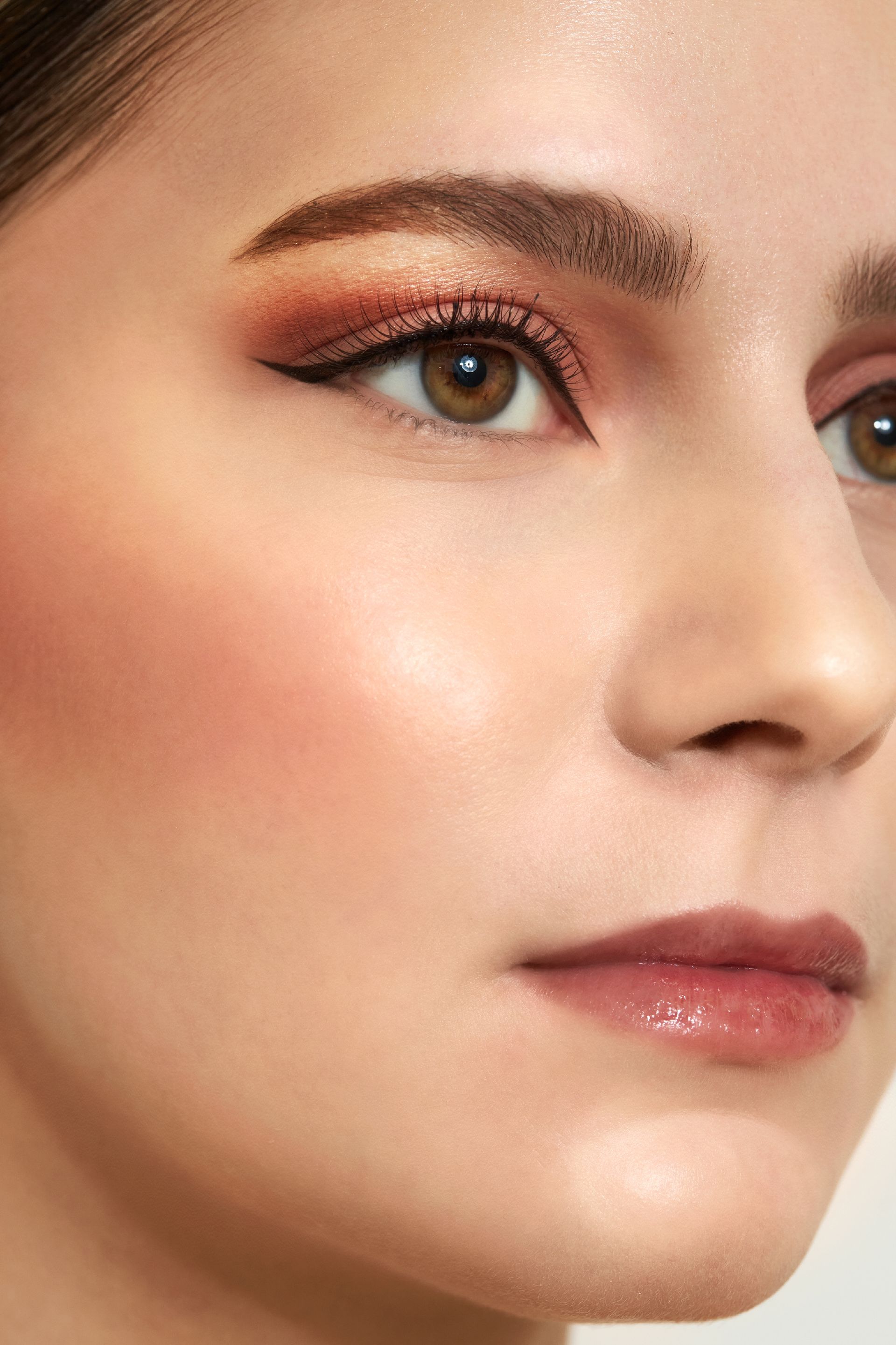 Frau mit braunen Augen und Make-up in warmen Tönen, einschließlich Lidschatten, Rouge und Lipgloss.