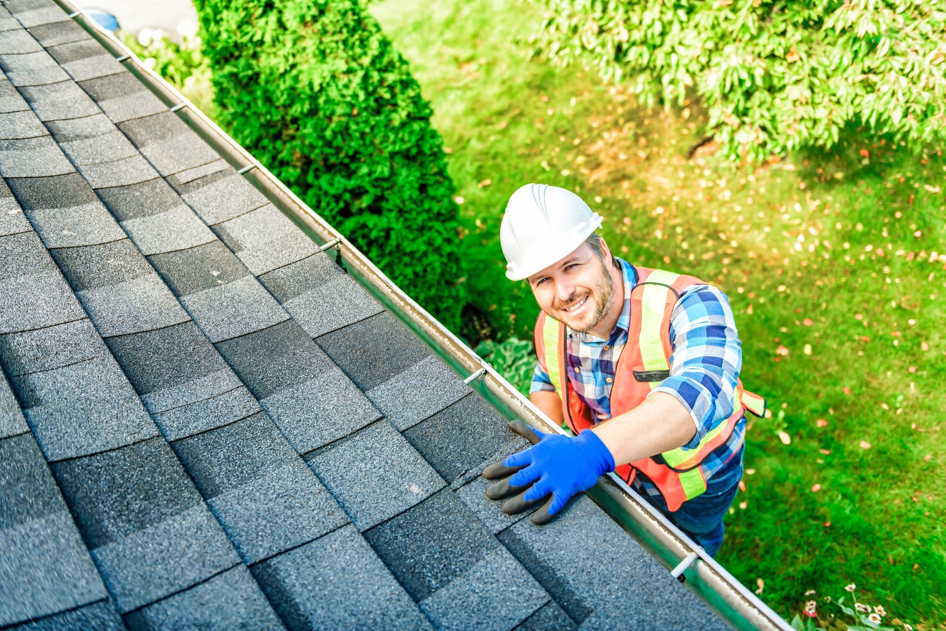 Roofer in white helmet on roof, inspecting metal panels, sunny day.