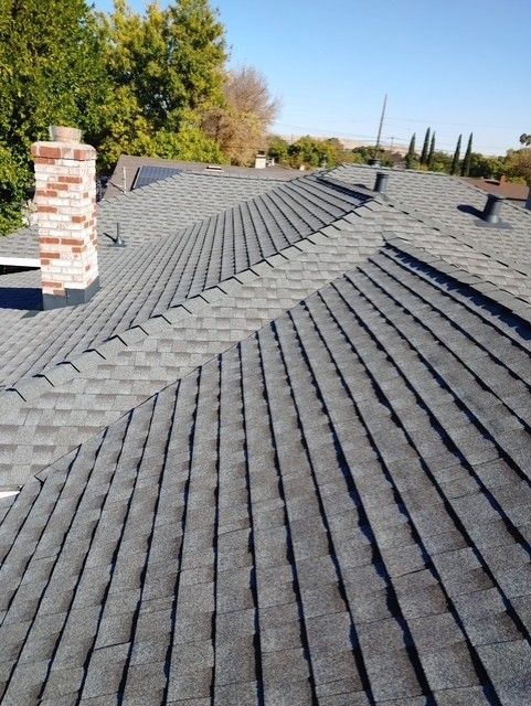 Gray shingle roof with a brick chimney under a blue sky; residential neighborhood.
