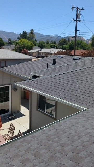 View of houses with a gray shingle roof and mountains in the distance on a sunny day.