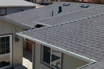 Flat roof under construction with chimney and windows, surrounded by green trees.