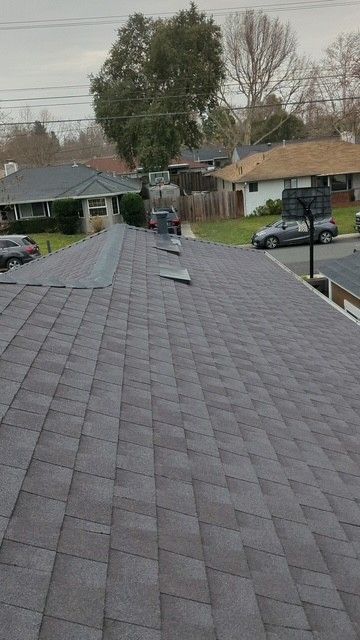 A gray asphalt shingle roof, with missing shingles and a tree in the background, in a suburban setting.