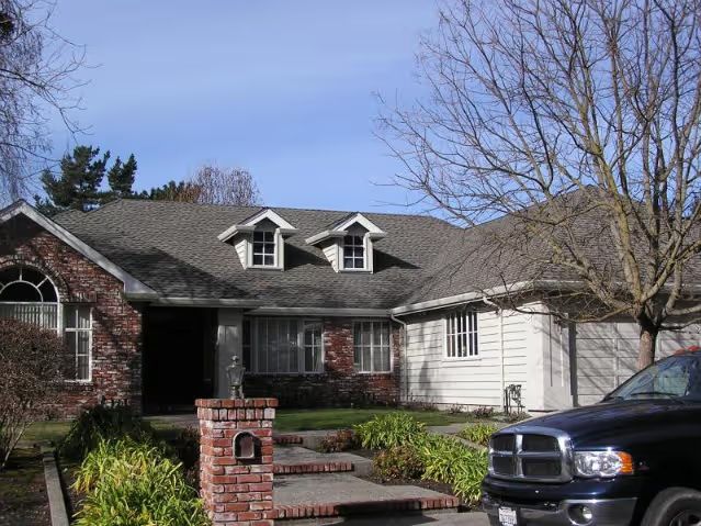 Brick house with gray roof, white car parked out front.