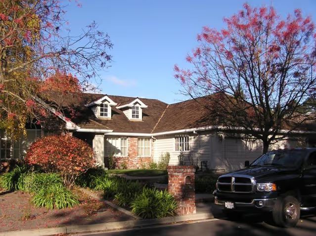 House under construction with exposed wooden frame, unfinished roof, and dirt pile in yard.