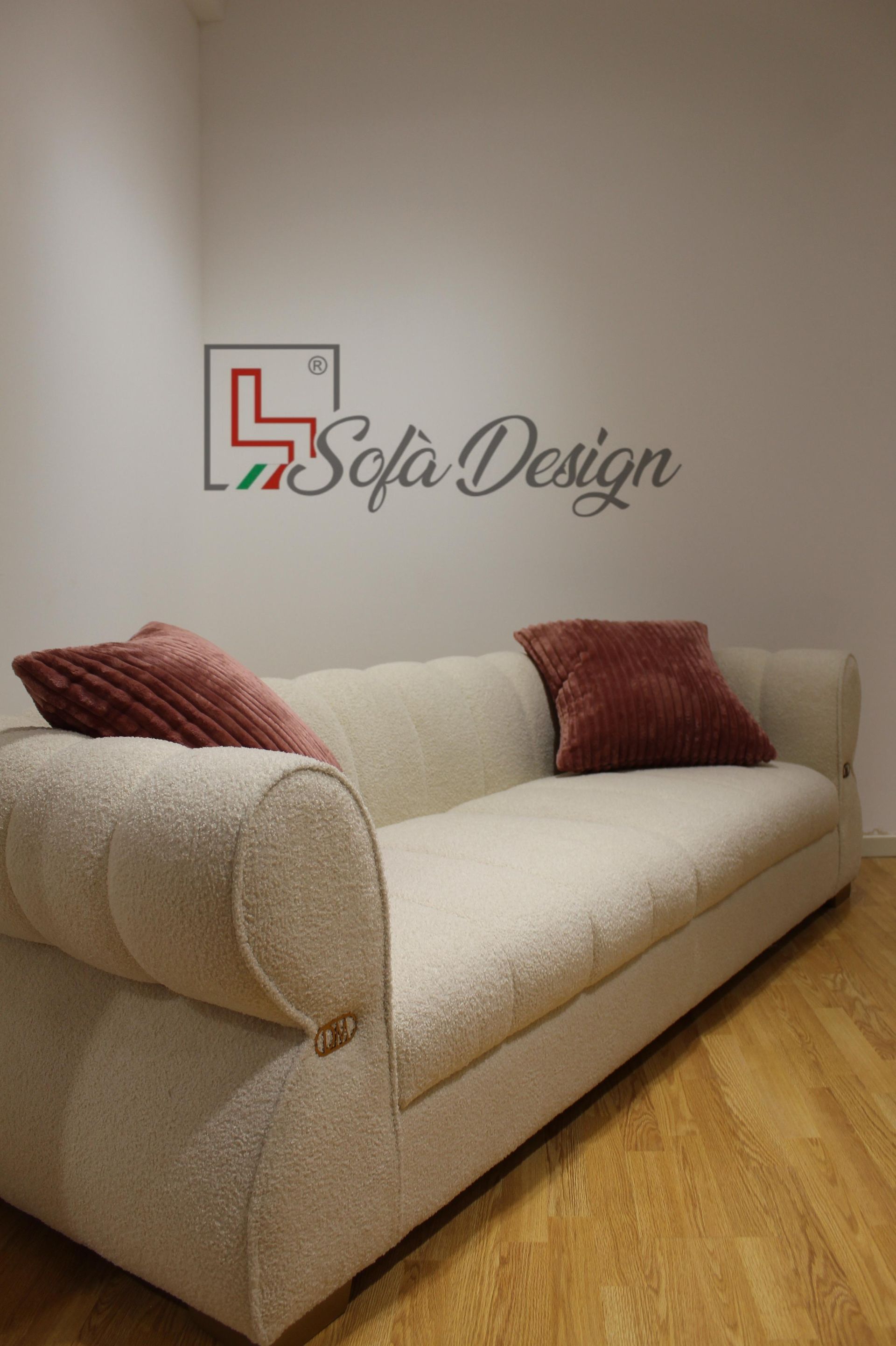 Divano in bouclé beige con due cuscini rosa contro una parete bianca con il logo 