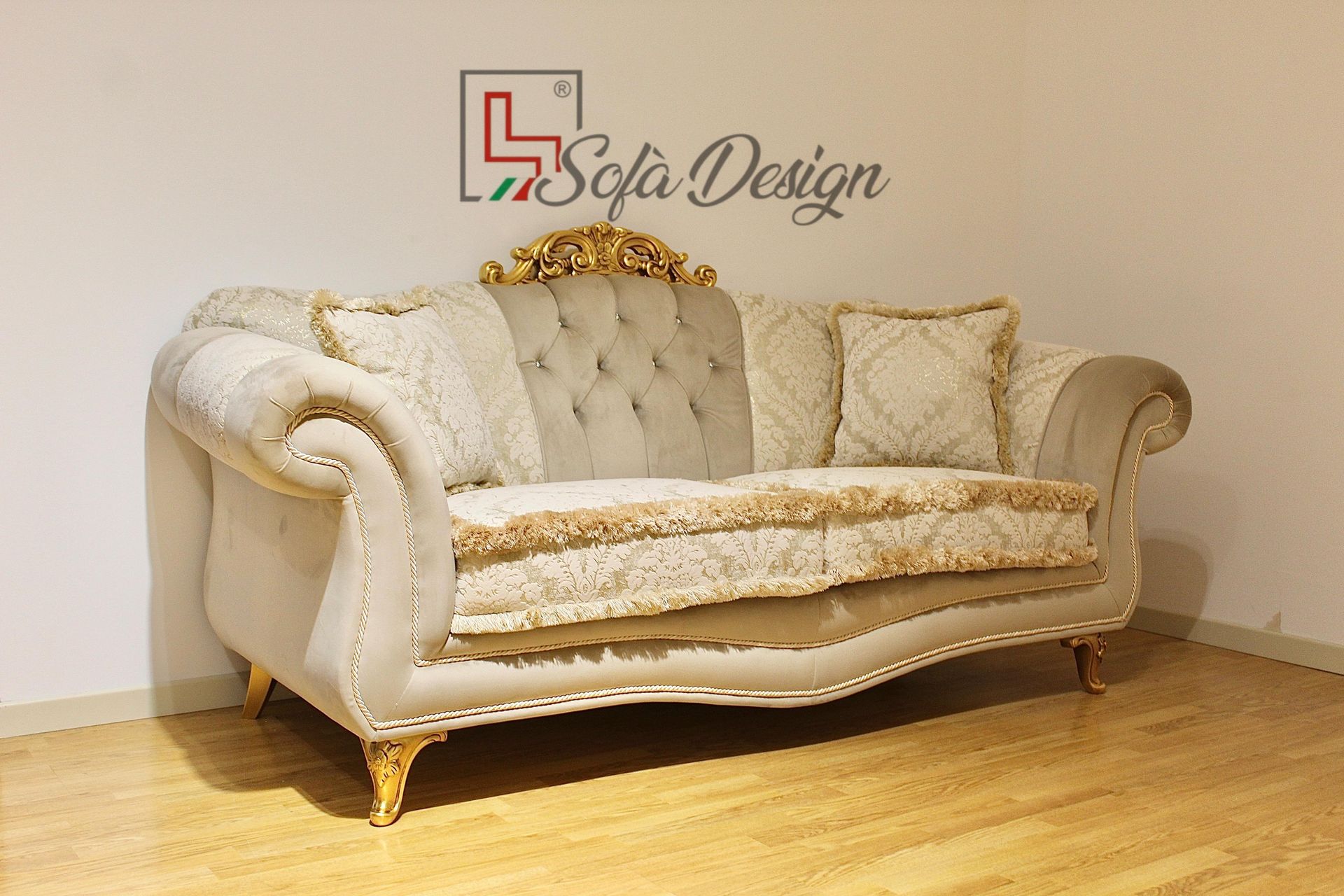 Divano beige decorato con dettagli dorati, appoggiato su una parete bianca e un pavimento in legno.