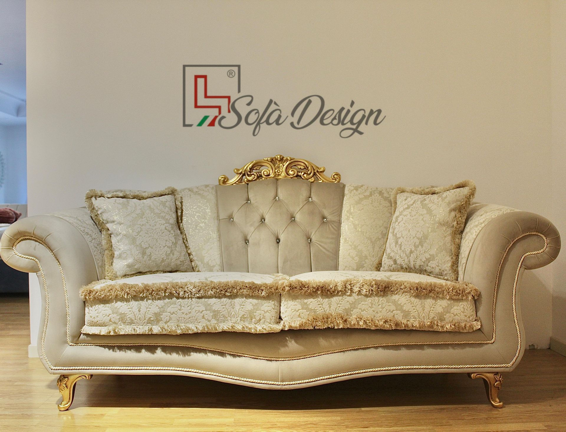 Divano beige decorato con dettagli dorati, due cuscini e rifiniture decorative.