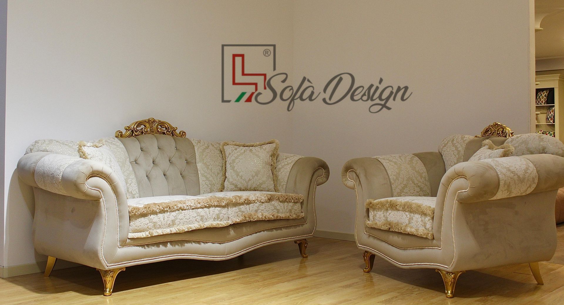 Divano e poltrona beige con dettagli dorati, di fronte a una parete bianca con il logo 