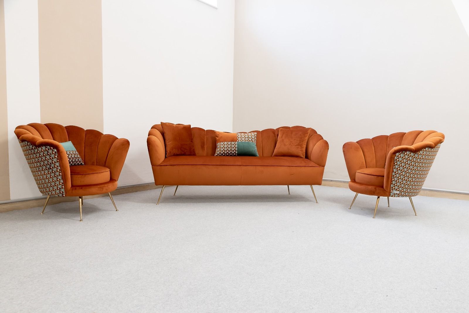 Divano e poltrone in velluto arancione con gambe dorate, sistemati in una stanza con un tappeto color crema.