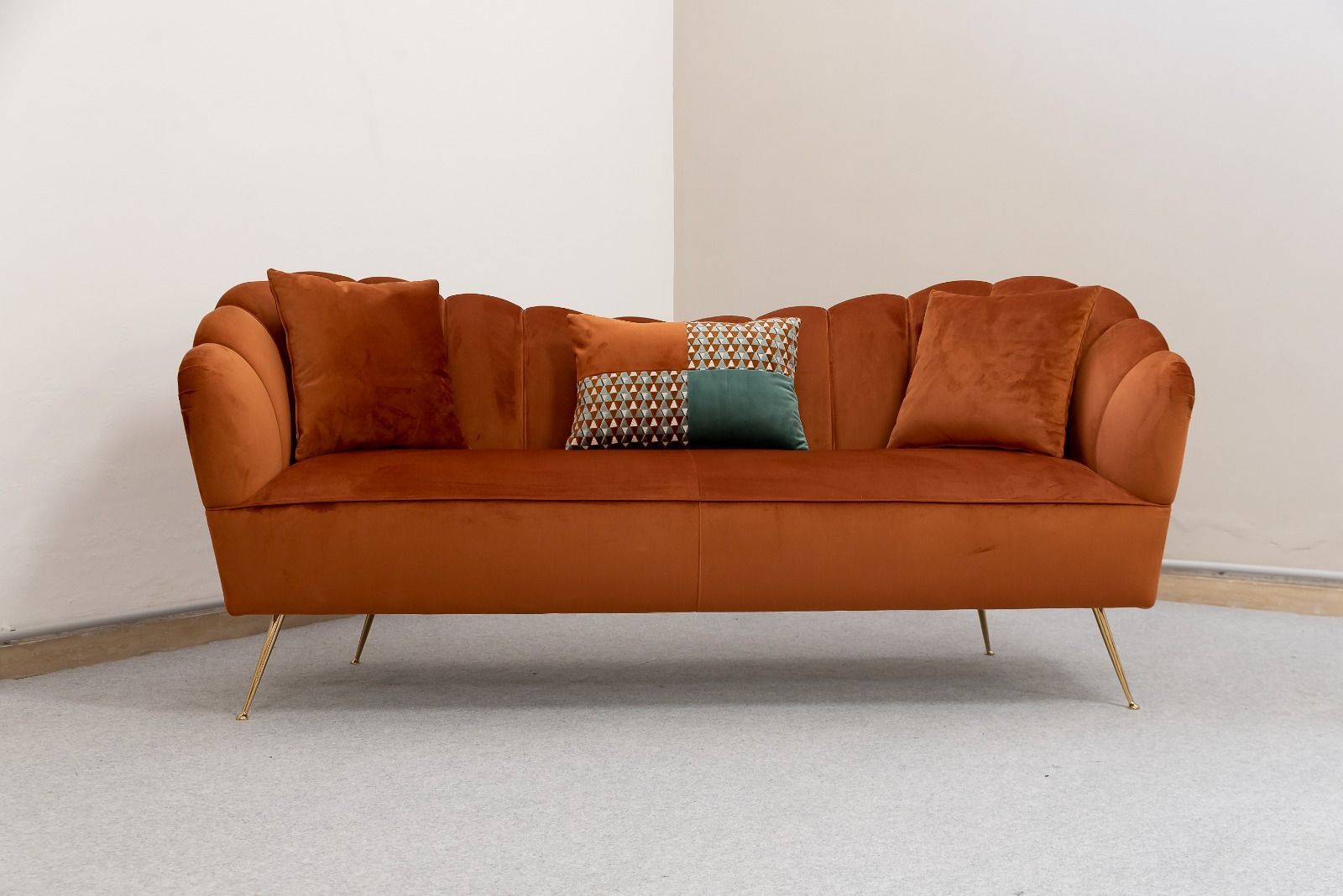 Divano in velluto arancione con gambe dorate, schienale smerlato e cuscini decorativi in ​​un angolo.