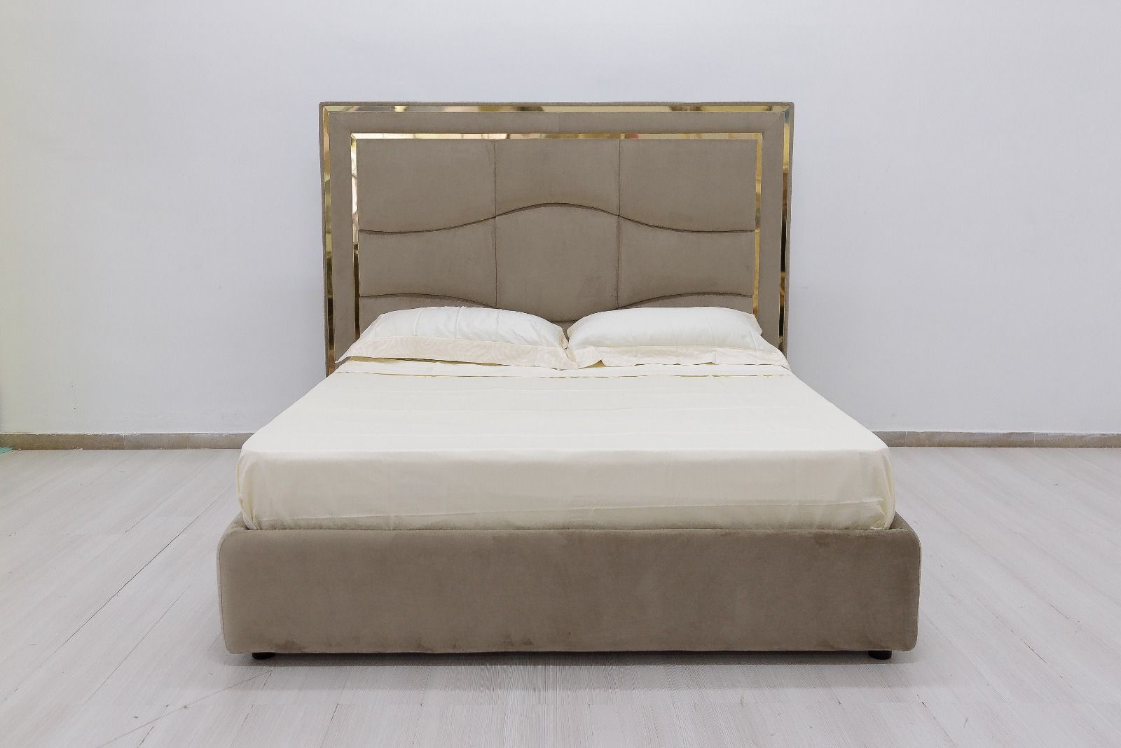 Letto imbottito beige con testiera decorativa in una stanza bianca.