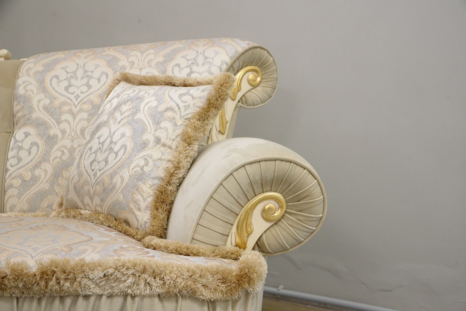 Primo piano del bracciolo di un divano di lusso con dettagli decorati a volute, frange e rivestimento a fantasia.