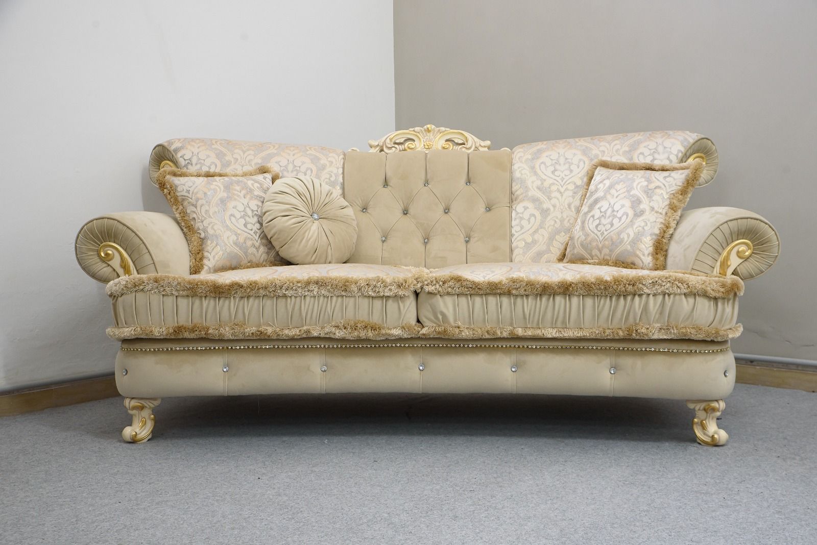 Divano decorato nei toni del beige e dell'oro con cuscini decorativi, appoggiato a una parete neutra.