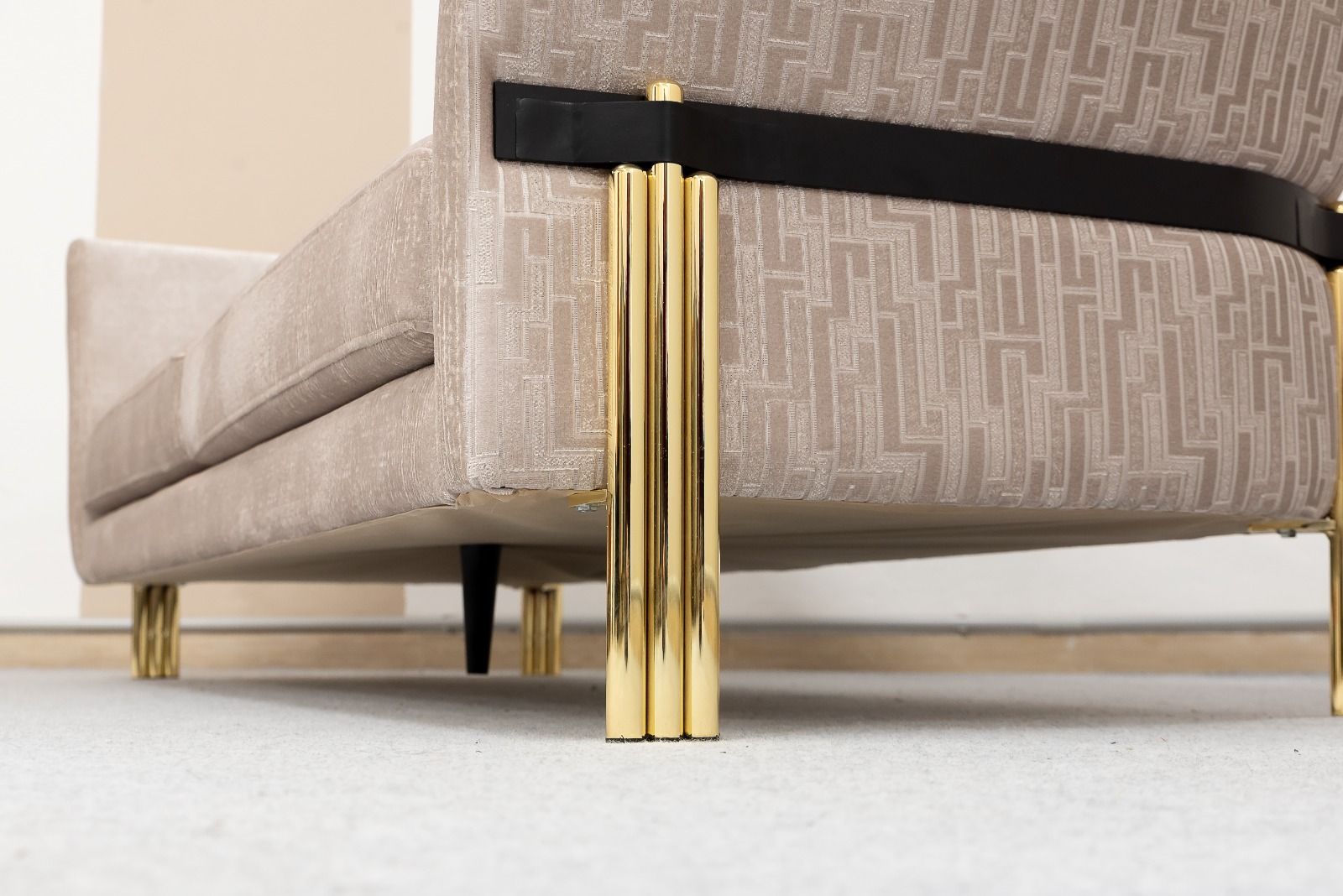 Divano beige con gambe cilindriche dorate contro una parete neutra.
