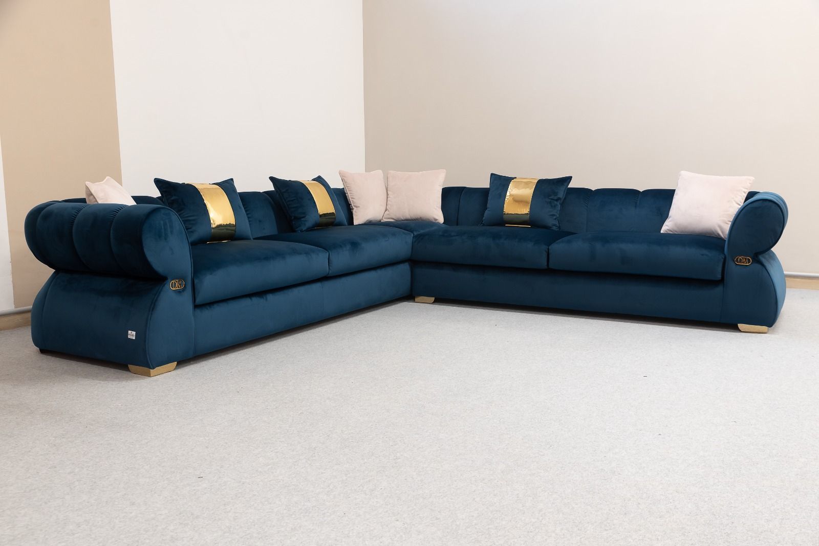 Divano componibile in velluto blu con dettagli e cuscini dorati, in una stanza dalle pareti bianche.