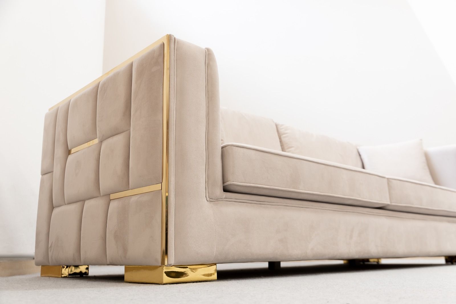 Divano in velluto beige con dettagli dorati in una stanza ben illuminata.