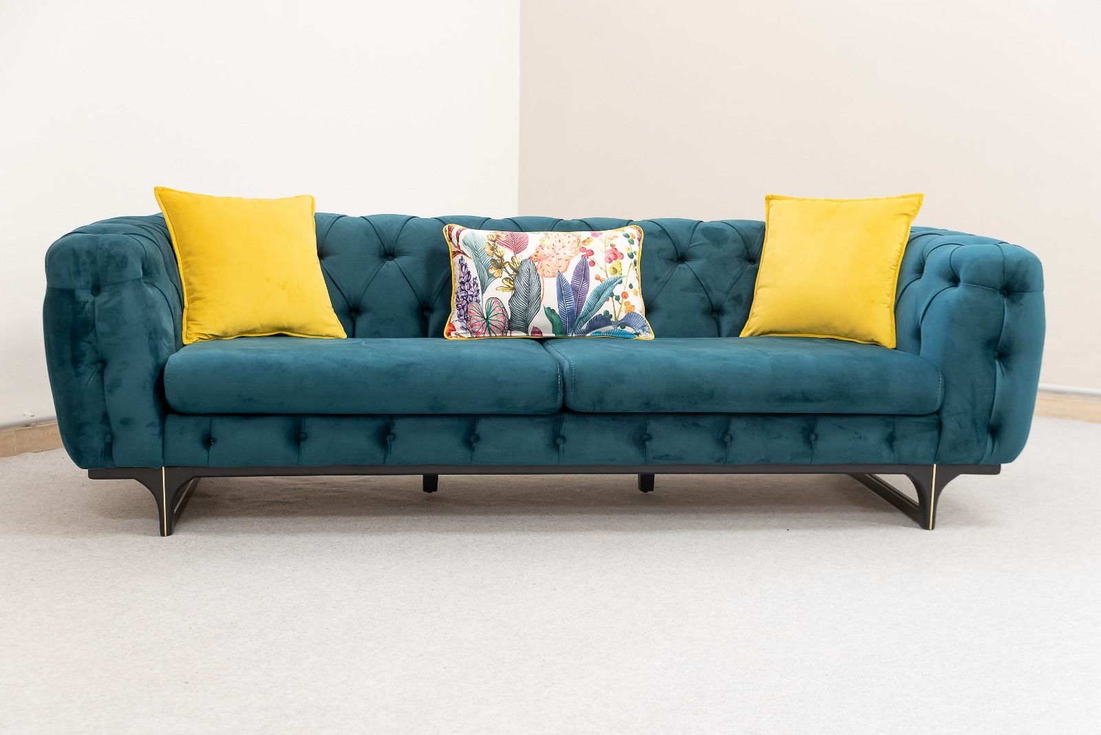 Divano capitonné color verde acqua con cuscini gialli e floreali contro una parete bianca.