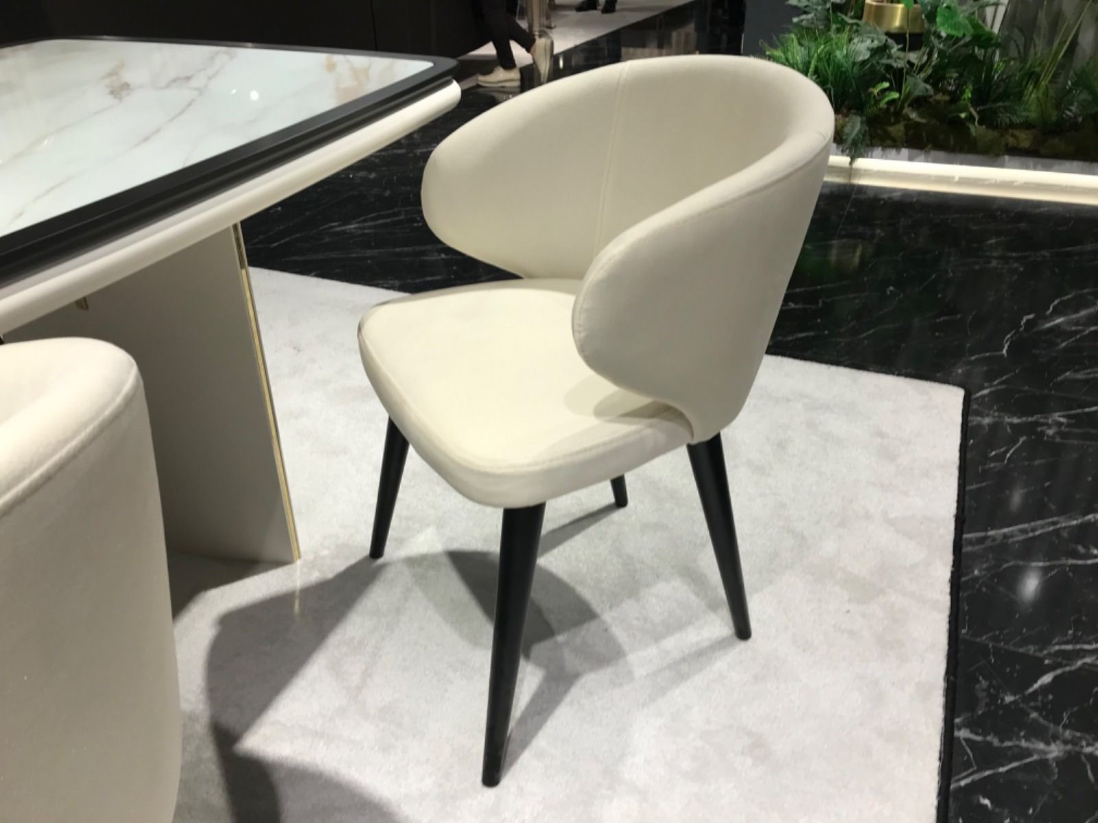 Sedia da pranzo color crema con gambe nere, accanto a un tavolo. L'ambiente è all'interno, su un tappeto chiaro.