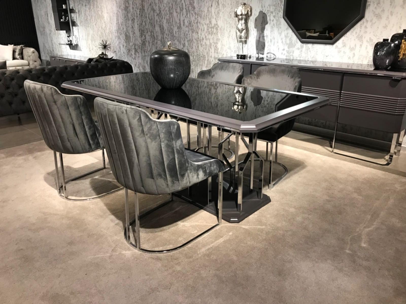 Sala da pranzo con tavolo in vetro nero, sedie argentate e credenza nera.