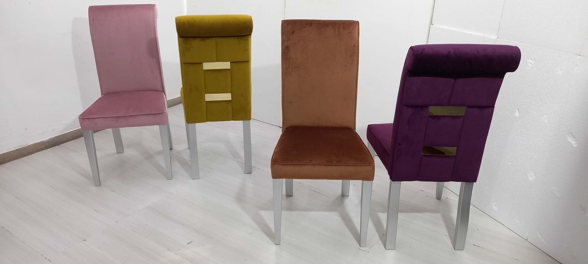 Quattro sedie in velluto rosa, giallo, marrone e viola con gambe argentate.