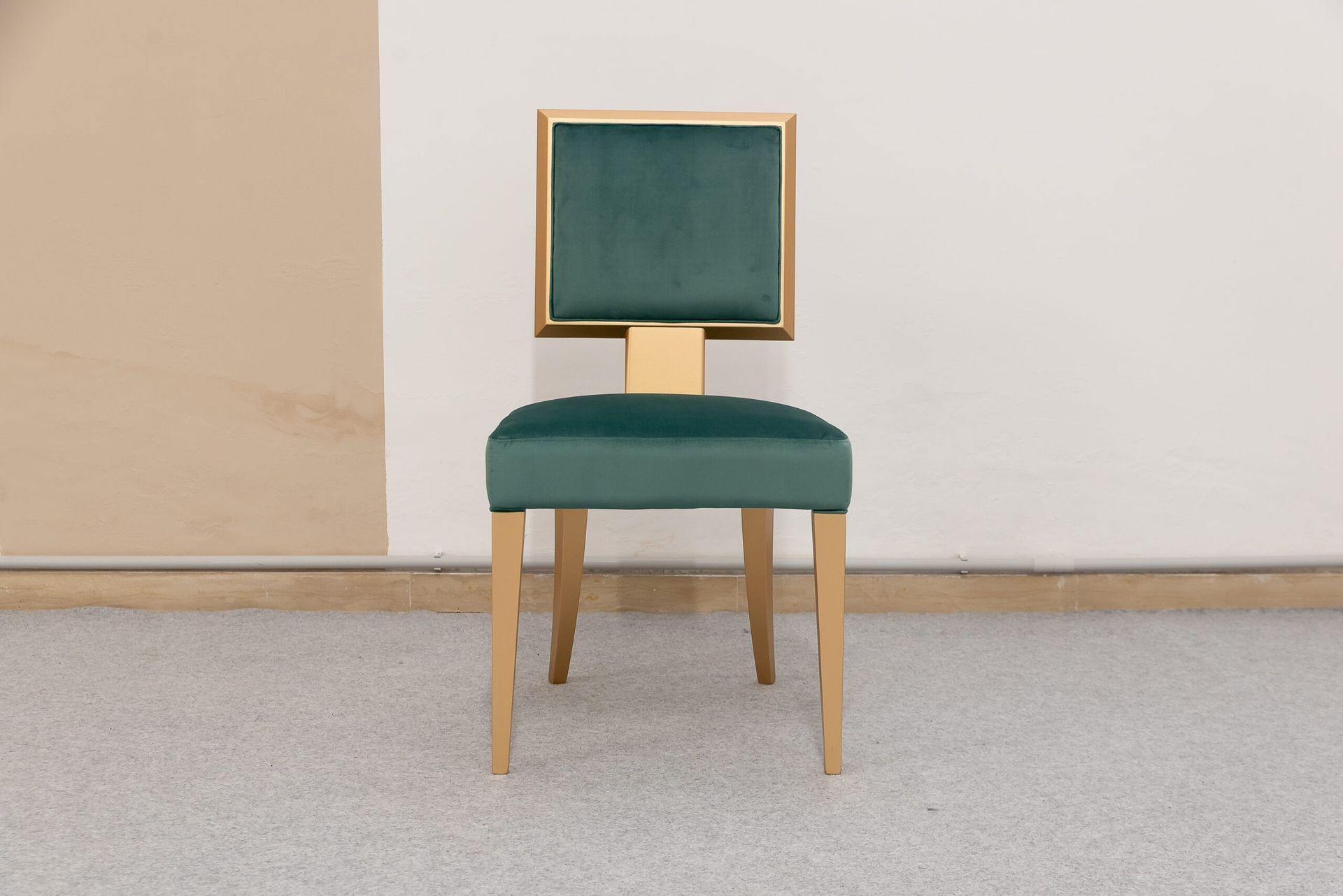 Sedia in velluto verde con finiture dorate e gambe in legno su un pavimento punteggiato.