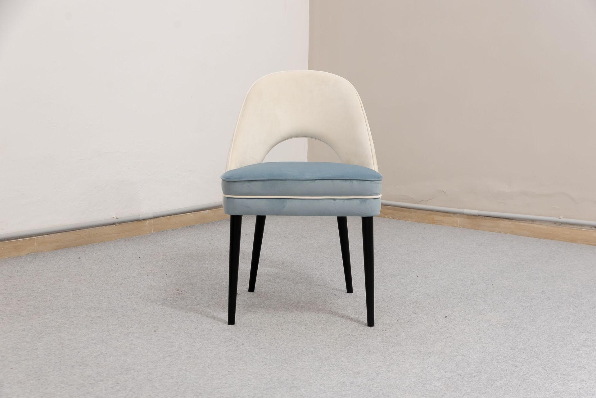 Sedia imbottita color crema e blu con gambe nere in un angolo di una stanza.