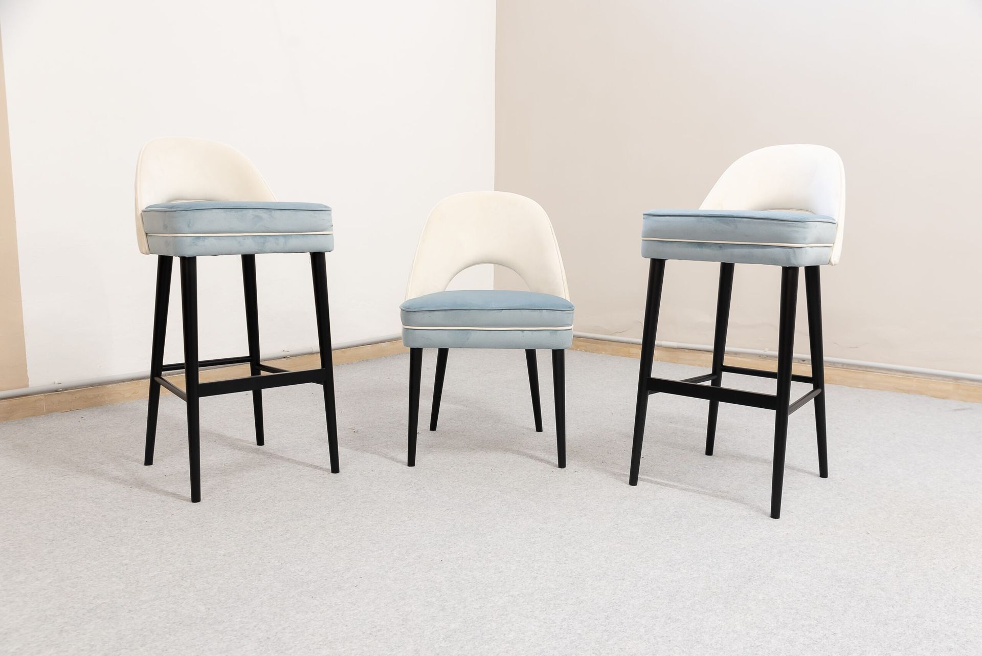 Tre sgabelli da bar con gambe nere, sedute blu e schienali bianchi, in una stanza con moquette e pareti chiare.