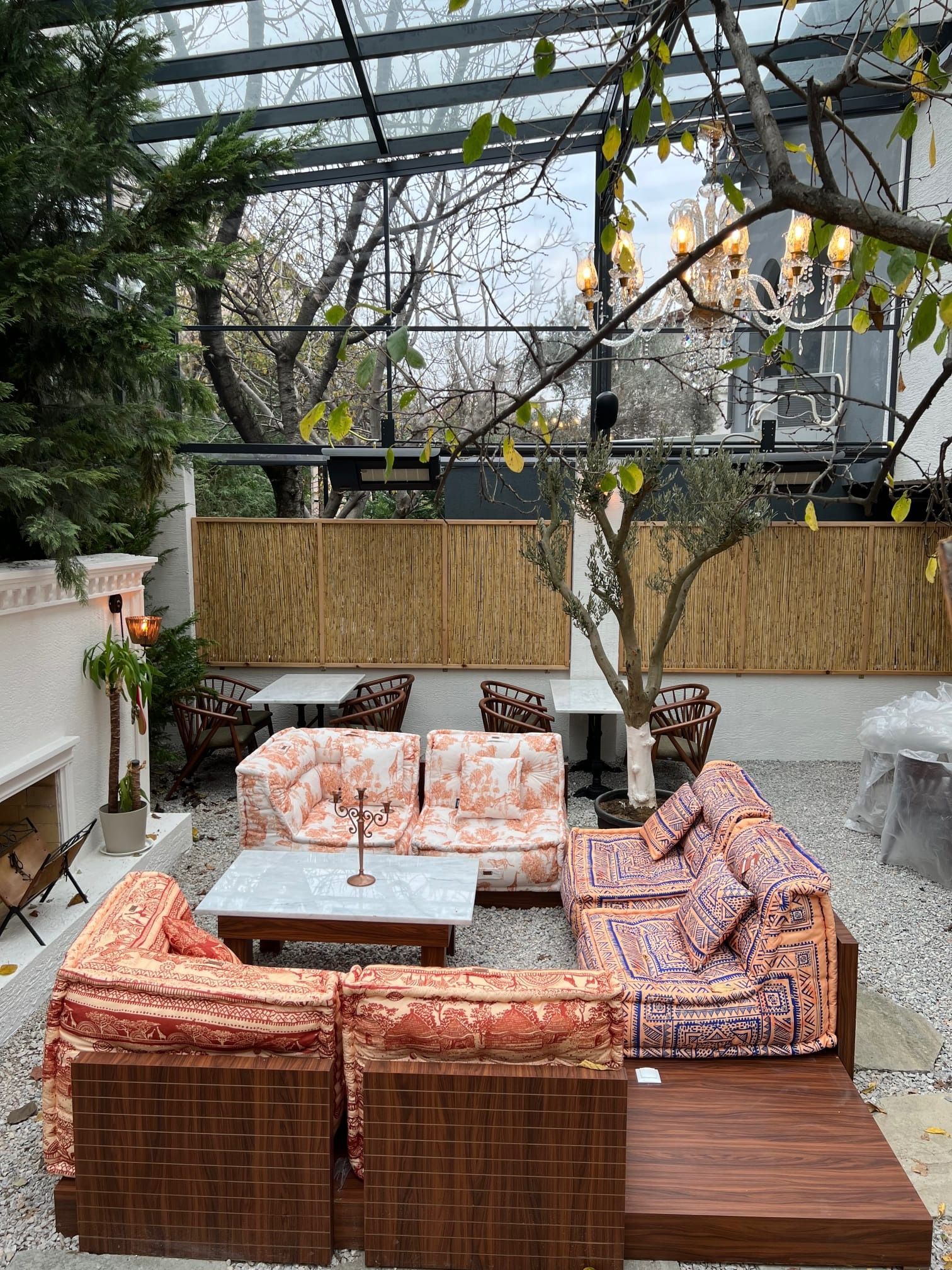 Area salotto all'aperto con divani decorati, tavoli e tetto in vetro.