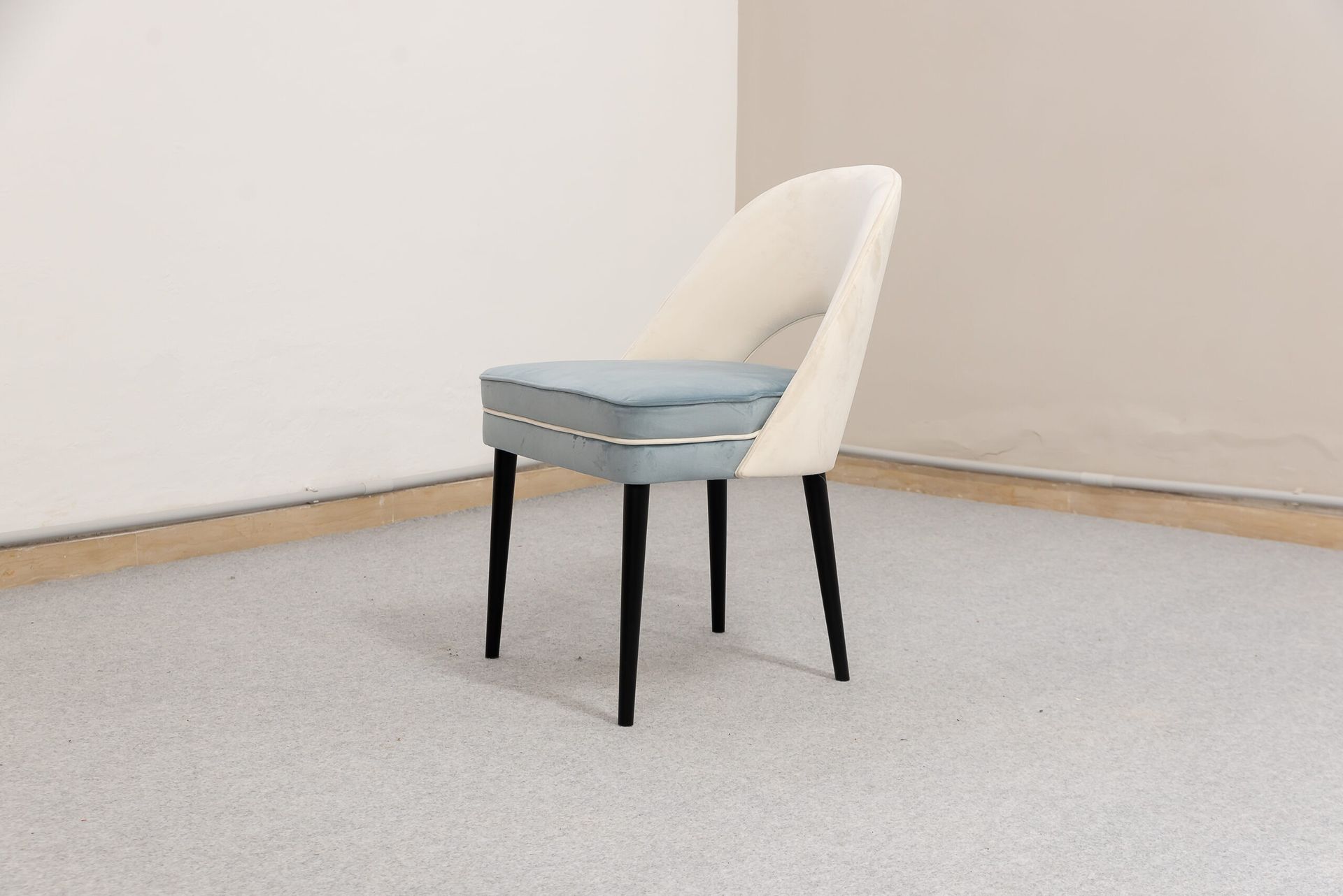 Sedia imbottita bianca e blu con gambe nere in una stanza dai toni neutri.