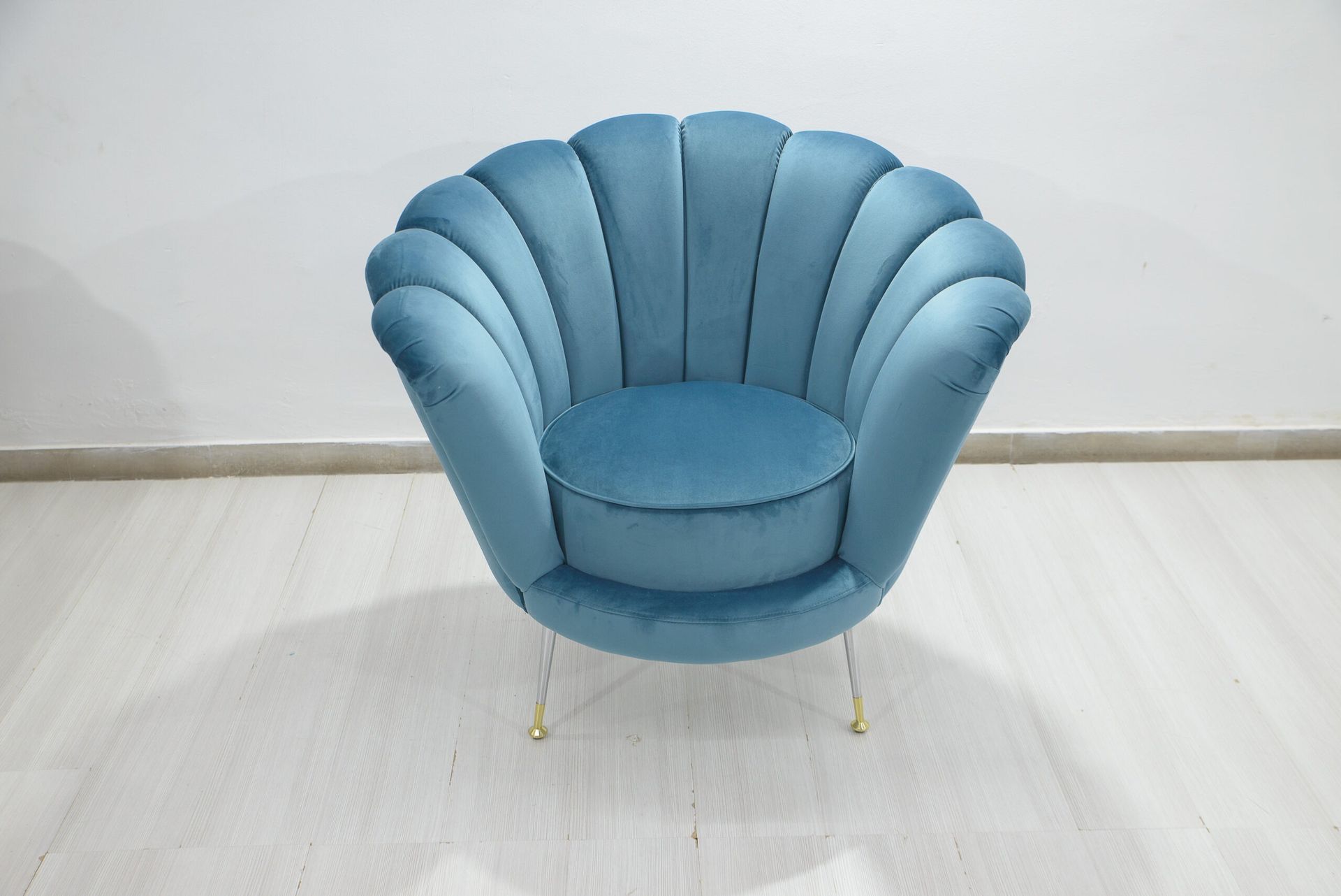 Poltrona a conchiglia in velluto blu con gambe dorate in una stanza dai colori chiari.