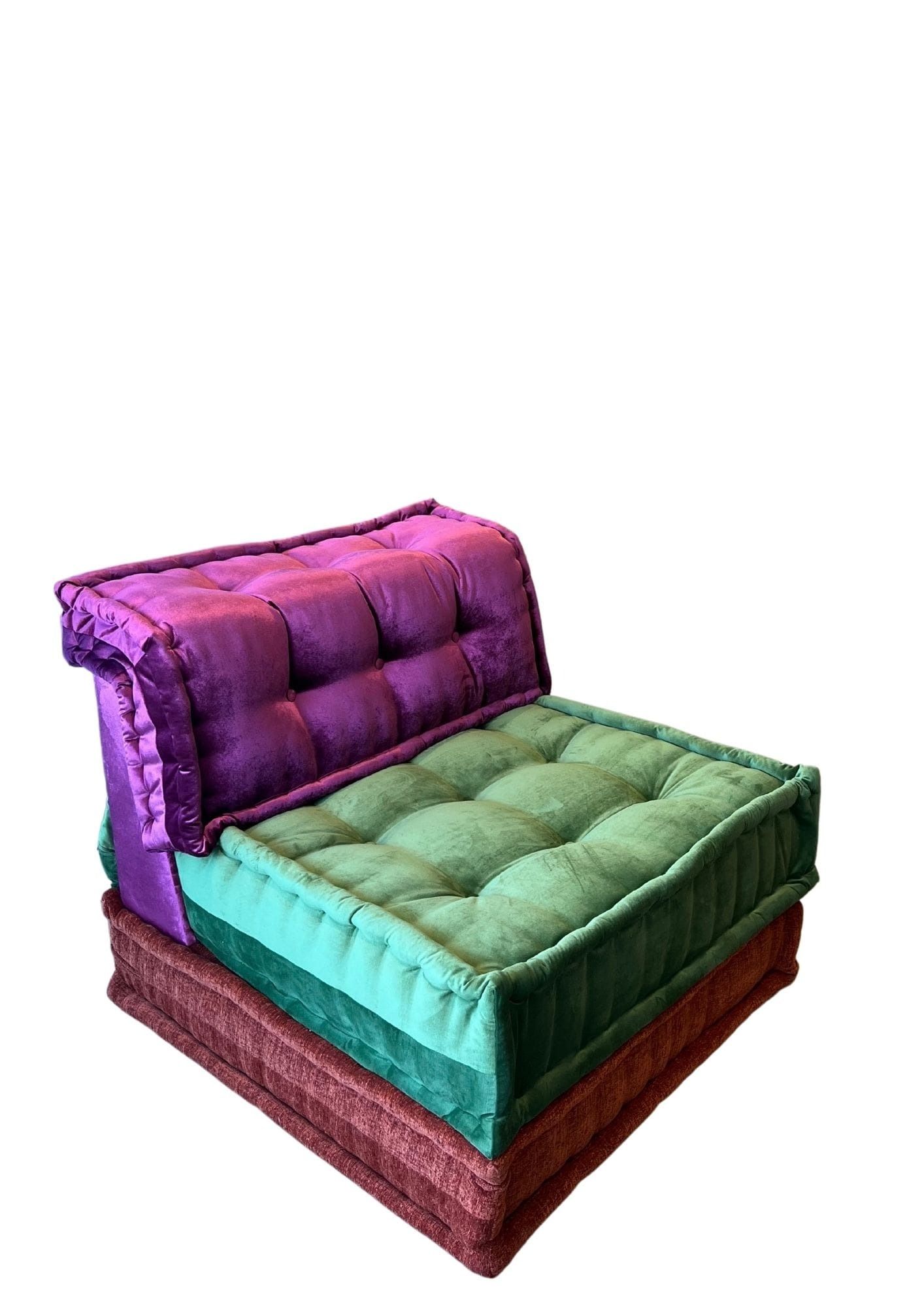 Poltrona con cuscini trapuntati colorati: schienale viola, seduta verde, poggiata su cuscini rossi e verdi sovrapposti.