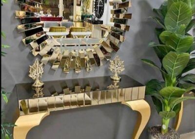 Specchio dorato e consolle decorata con elementi a specchio, di fronte a una parete grigia.