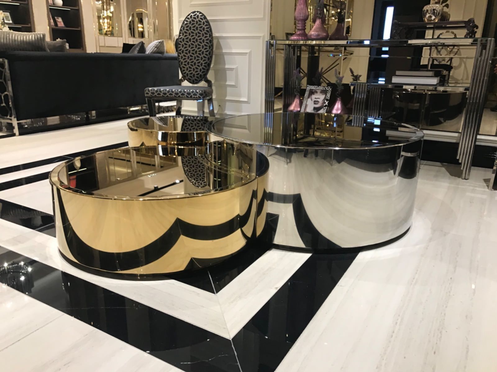 Tavolini da caffè circolari dorati e argentati su un pavimento piastrellato bianco e nero, in un ambiente moderno.