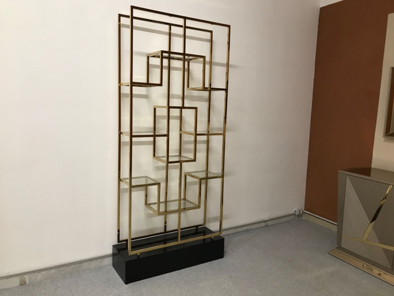 Mensola in metallo dorato e legno nero con motivo geometrico su pareti bianche e marroni.