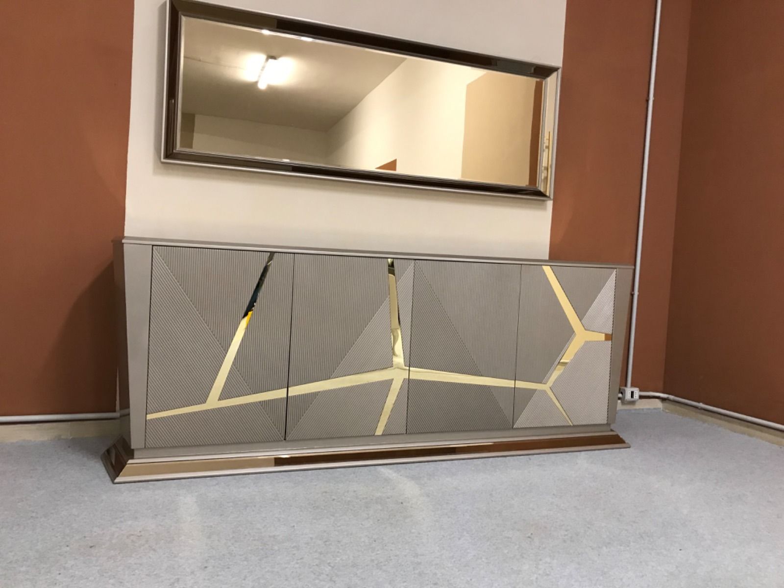 Credenza grigia con dettagli geometrici dorati, sotto uno specchio rettangolare.