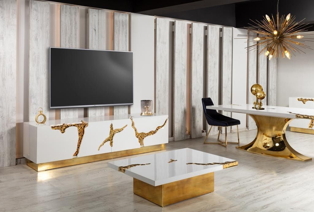 Soggiorno moderno con mobili bianchi e dorati, TV a schermo piatto a parete.