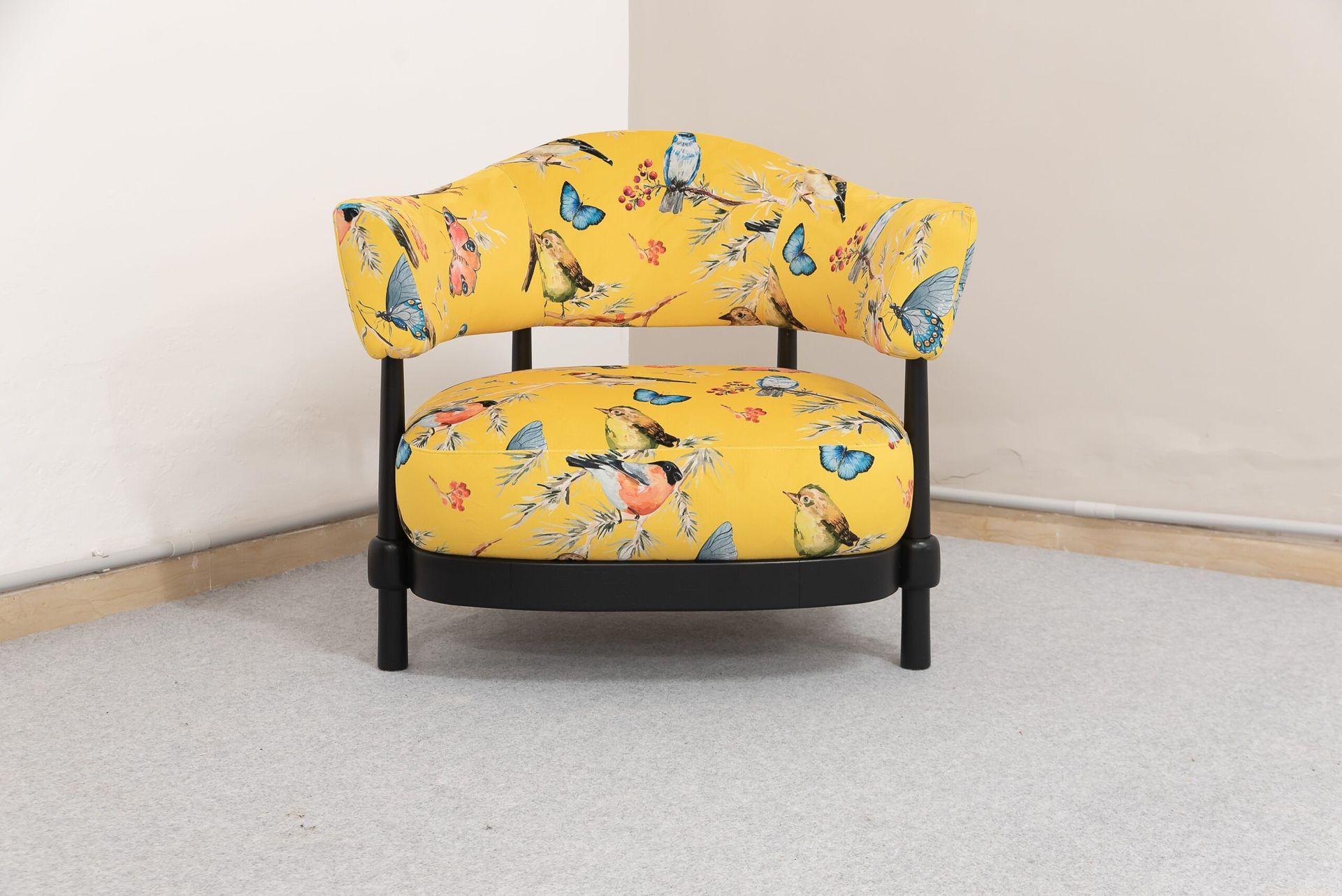 Poltrona gialla con stampa di uccelli e farfalle, struttura nera, in un angolo.
