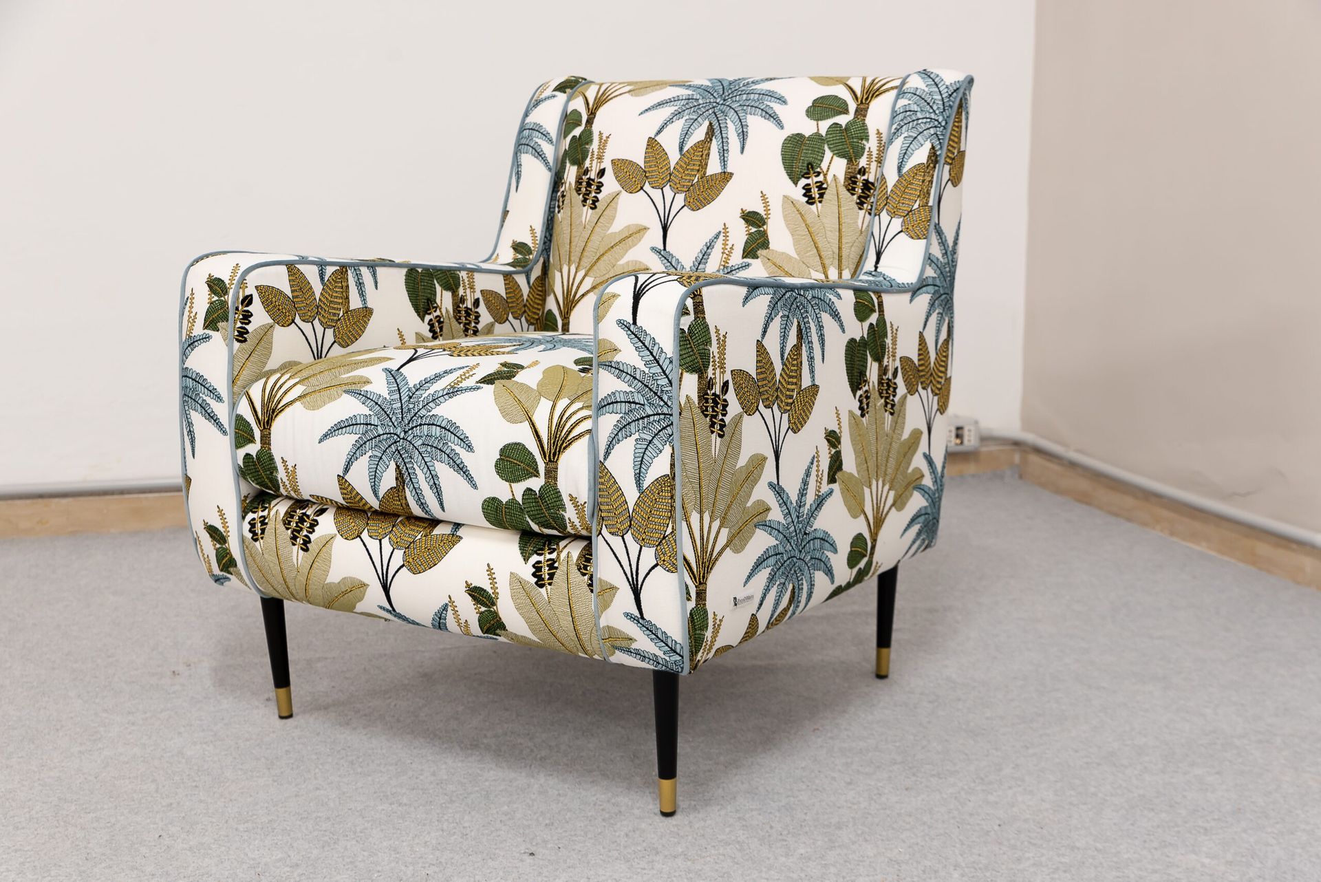 Poltrona con tessuto a motivi floreali e vegetali, gambe nere con punte dorate e sfondo bianco.