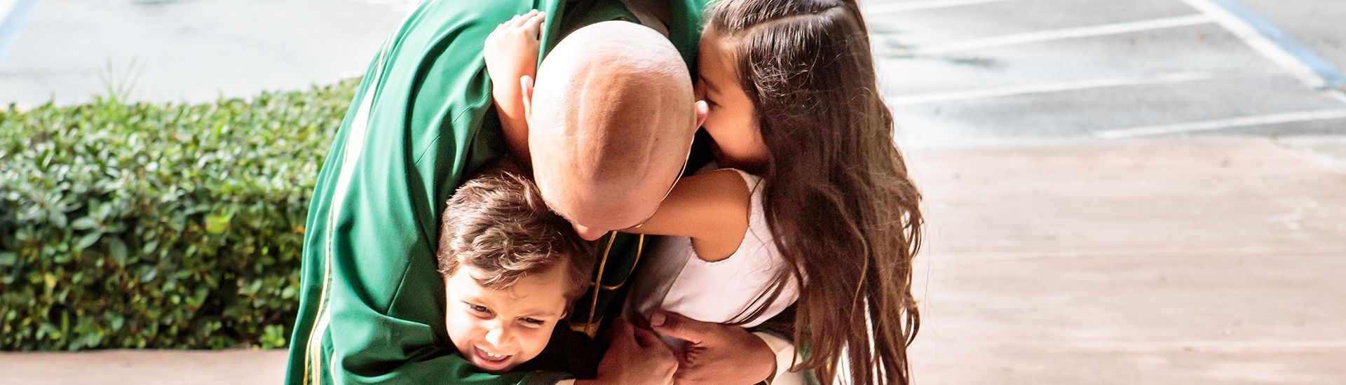 A man in a green jacket is kissing two children on the cheek.