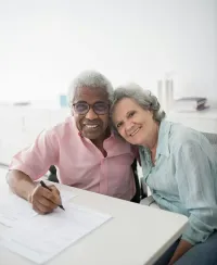 Three healthcare professionals in masks talking with a patient at a desk in a bright clinic