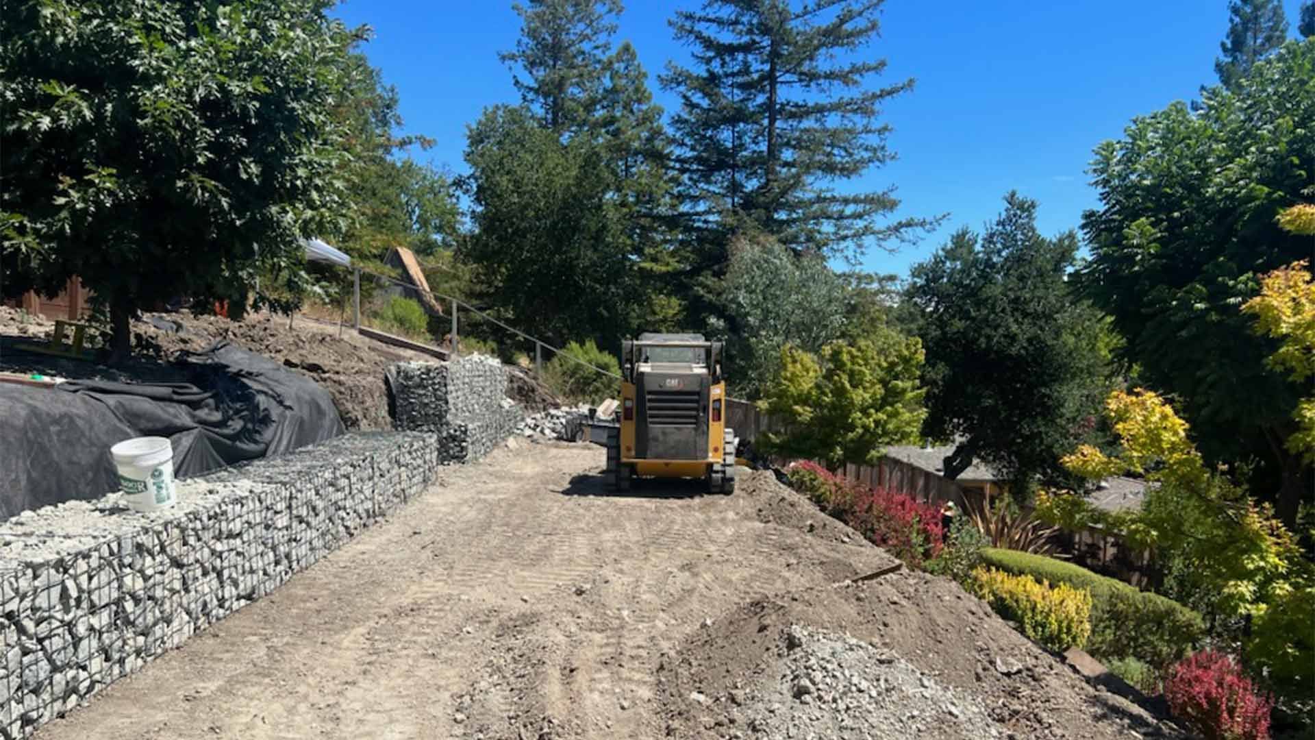 A bulldozer is driving down a dirt road next to a stone wall.