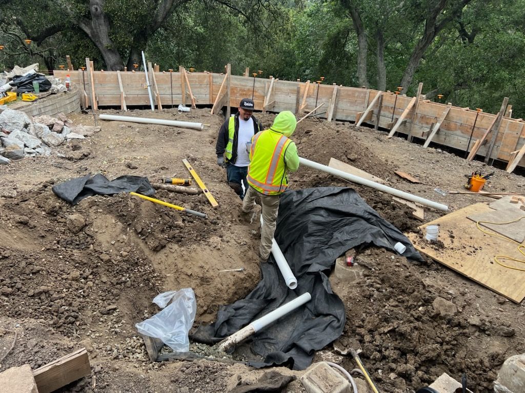 Two construction workers are standing in a dirt field.
