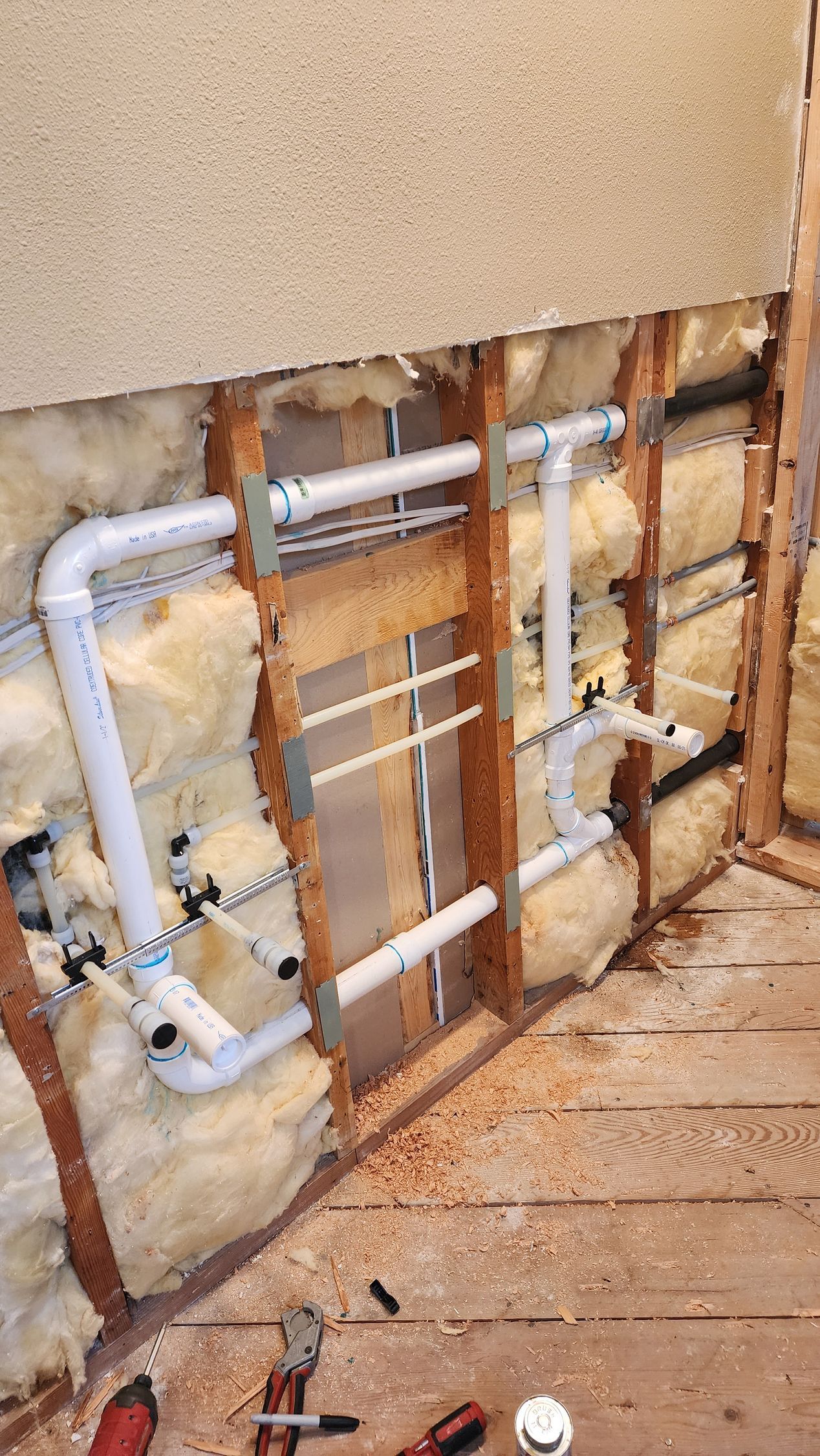Plumbing pipes and insulation installed within a wooden wall frame.