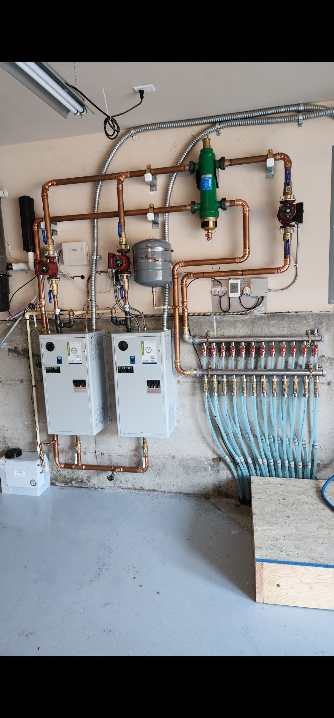Plumber in green overalls and gloves working on pipes, near a water heater and gauges.