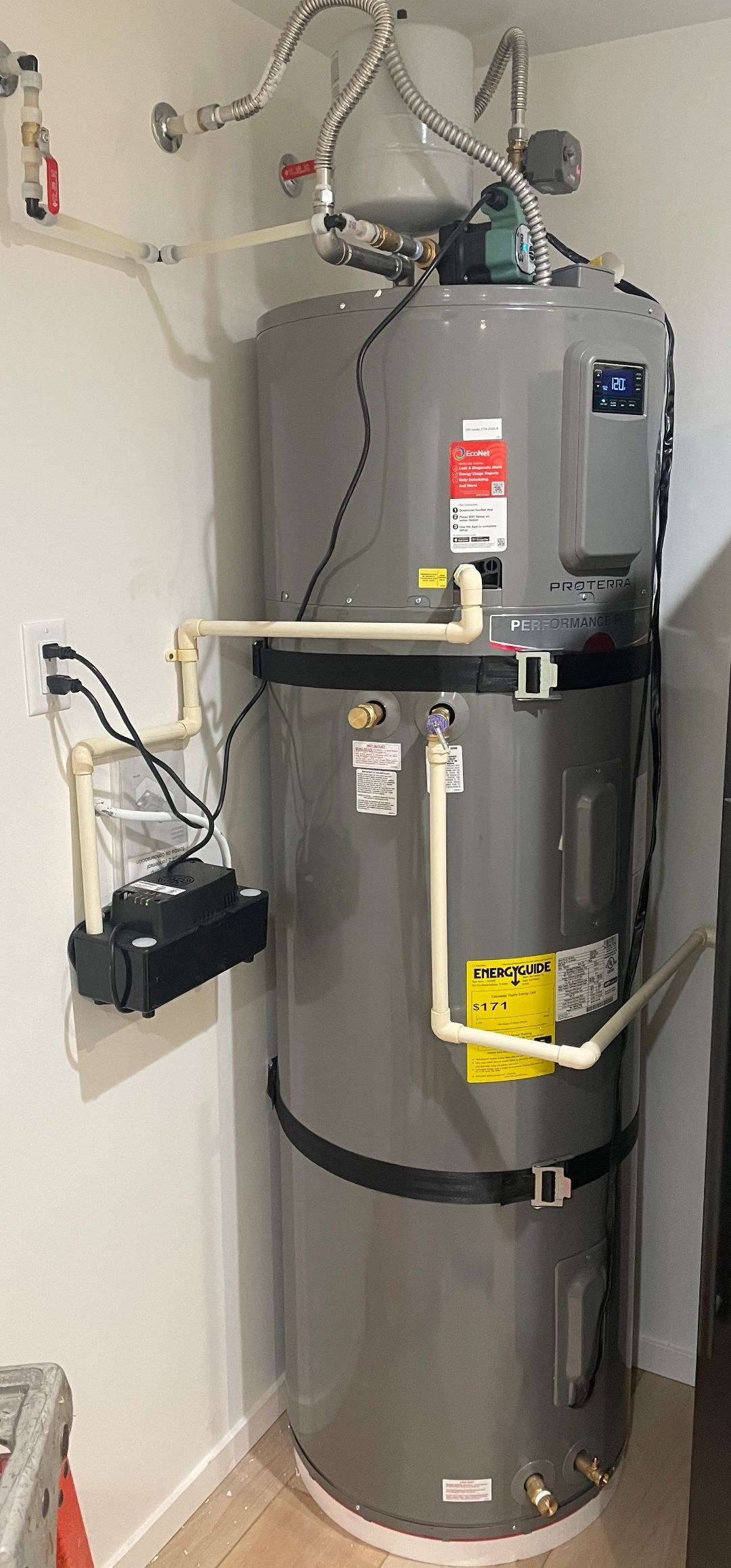White water heater against a brick wall, connected with pipes.
